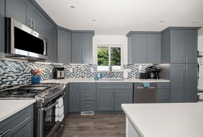 A modern kitchen with grey cabinets, a stainless steel range, and a tiled backsplash.