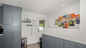 A modern kitchen with grey cabinets, a white countertop, and a wall-mounted artwork. - Updated Spacious Home & Hot Tub (Spokane Valley)