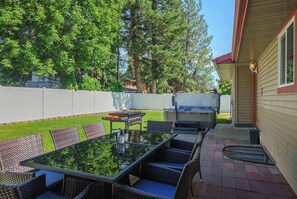 Un patio al aire libre con una mesa de vidrio, sillas de mimbre y una parrilla.