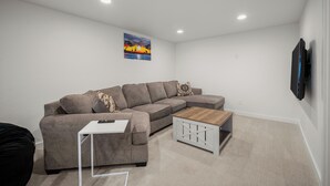A living room with a sectional sofa, a coffee table, a small white side table, and a painting on the wall. - Updated Spacious Home & Hot Tub (Spokane Valley)
