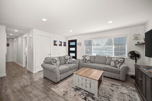A modern living room with a grey sofa set, a wooden coffee table, and a large window with blinds.