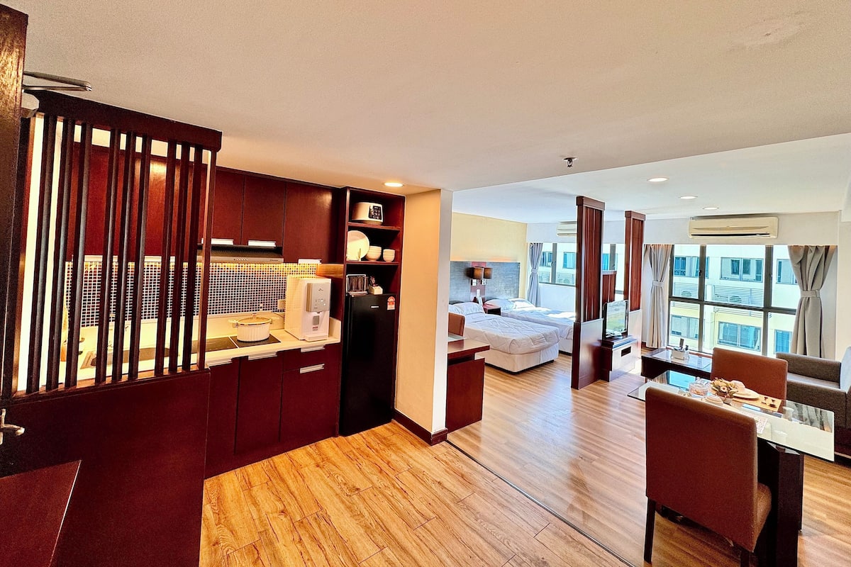 Una habitación de hotel moderna con kitchenette, zona de comedor y dormitorio con un ventanal grande.