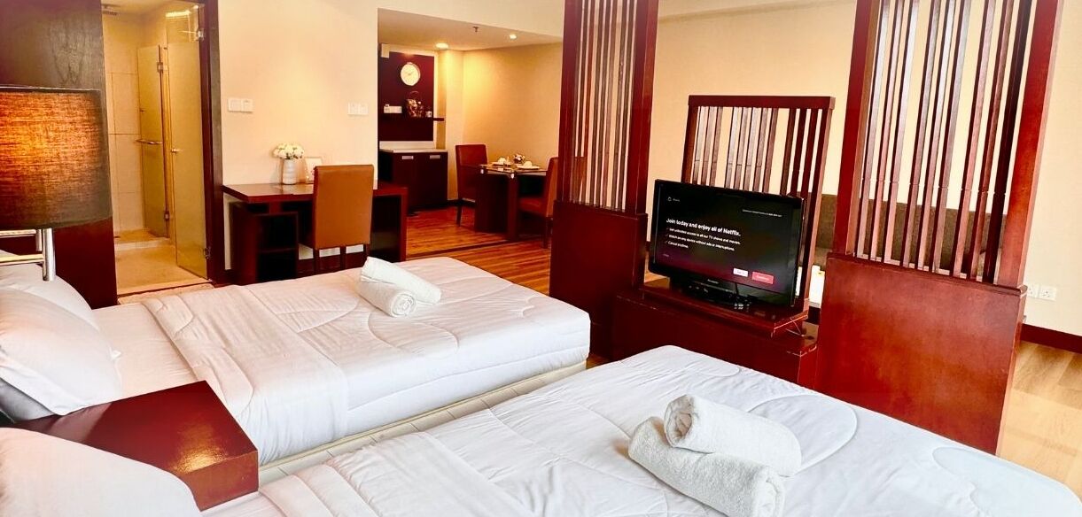 A hotel room with two beds, a TV, a desk, and a shower area.