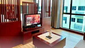 Habitación de hotel con una televisión sobre un mueble de madera, una mesita con un control remoto y una ventana que da a edificios.