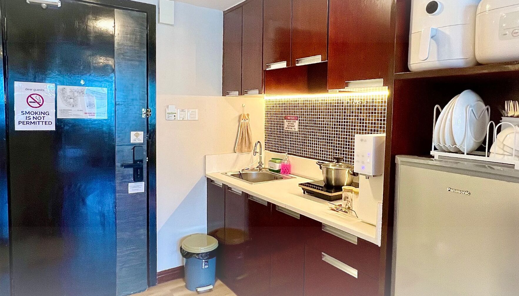 A compact kitchen with a refrigerator, sink, and a microwave. A no-smoking sign is visible on the door.