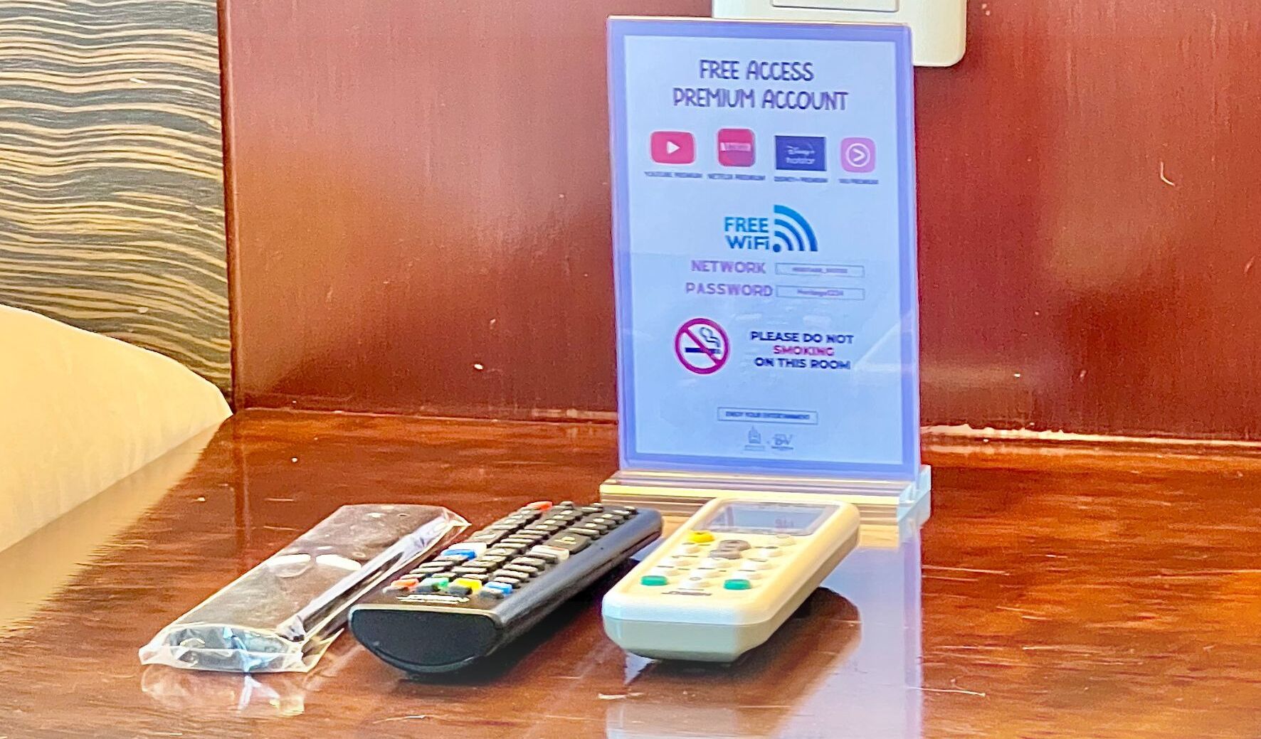 A sign for a free access premium account with a network password, a no-smoking sign, and two remote controls on a wooden surface.