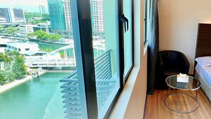 Habitación de hotel moderna con un amplio ventanal que ofrece vistas a un paisaje urbano y a un río.