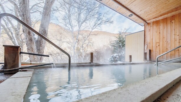 A hot spring area with a wooden interior, a concrete pool, and a view of trees and hills. - Shigakogen Milky Hot Spring Keikokunoyu (Yamanouchi)
