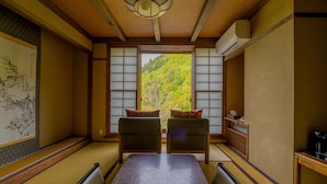 A traditional Japanese room with tatami flooring, a low table, two cushions, and a view of a forested hillside through shoji screens. - Shigakogen Milky Hot Spring Keikokunoyu (Yamanouchi)