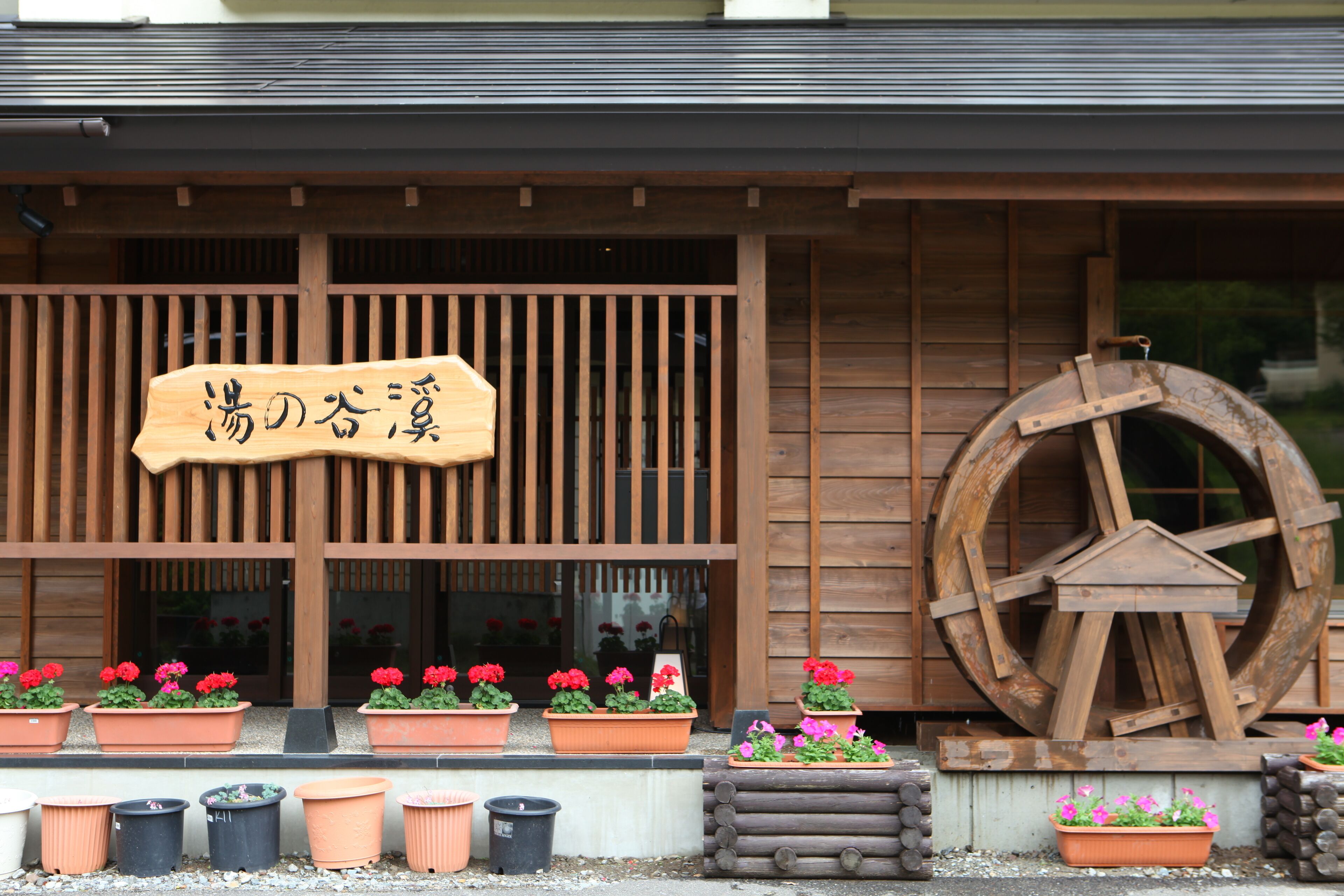 A traditional wooden building with a sign, potted plants, and a large wooden wheel.