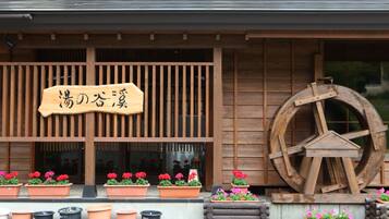 A traditional wooden building with a sign, potted plants, and a large wooden wheel.