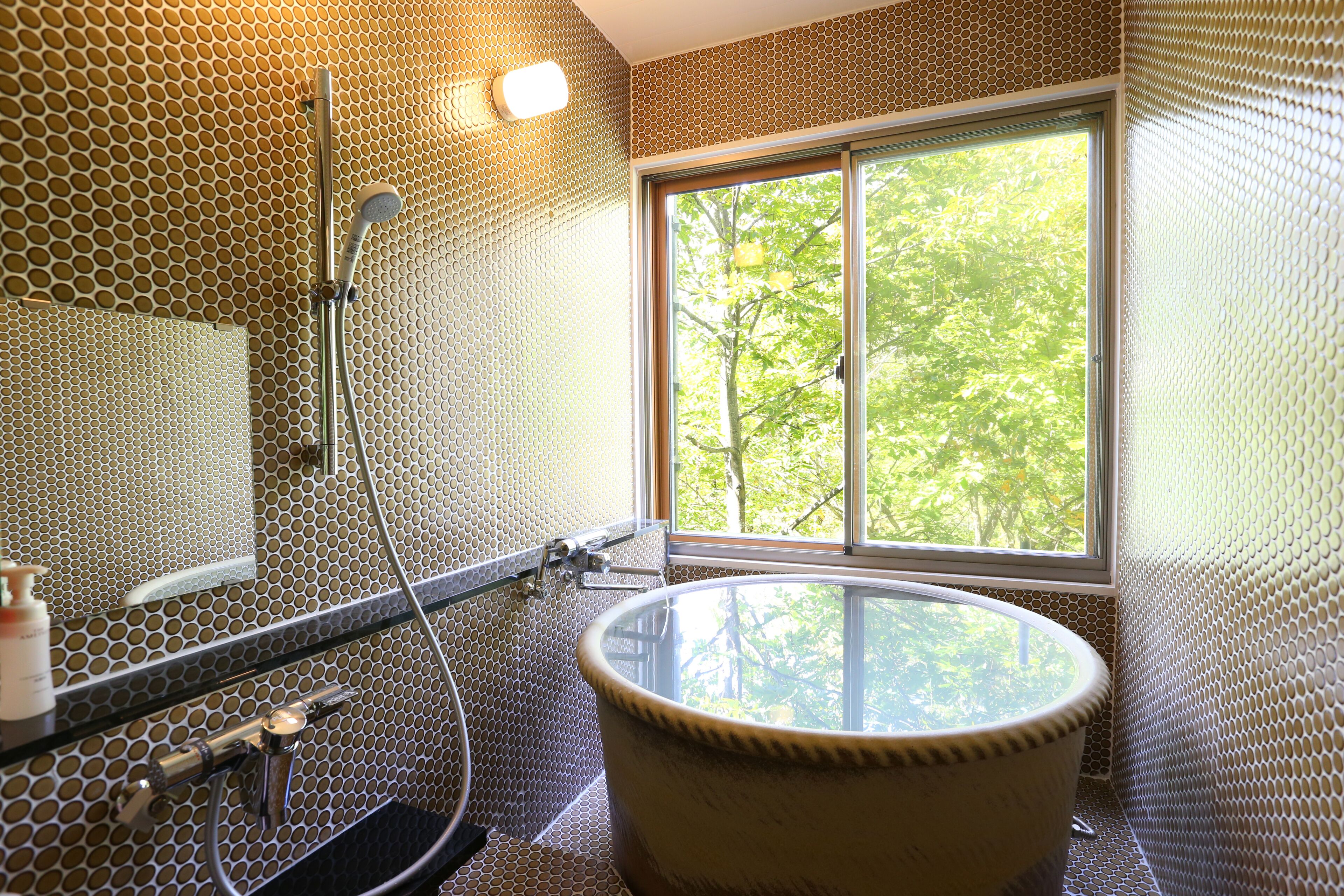 A bathroom with a large bathtub, a shower, and a window providing a view of trees.