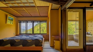 A traditional Japanese-style bedroom with tatami flooring, a bed, a sliding door leading to a bathroom, and a large window offering a view of a mountainous landscape. - Shigakogen Milky Hot Spring Keikokunoyu (Yamanouchi)
