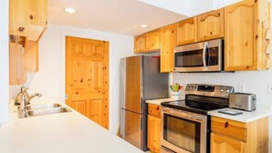 A kitchen with wooden cabinets, stainless steel appliances, a microwave, a refrigerator, an oven, and a sink. - Walkable everywhere with free parking and shared hot tub (Whistler)