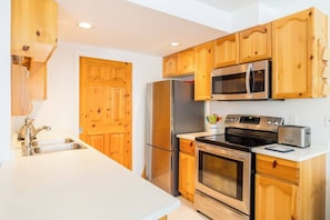 A kitchen with wooden cabinets, stainless steel appliances, a microwave, a refrigerator, an oven, and a sink.