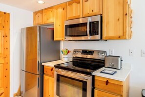 Eine kleine Küche mit Holzausstattung, einem Edelstahlkühlschrank, einer Mikrowelle, einem Backofen und einem Toaster.