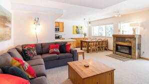 A living room with a sofa, coffee table, fireplace, dining area, and kitchen. - Walkable everywhere with free parking and shared hot tub (Whistler)