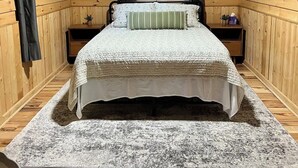 Una habitación con paneles de madera, una cama, una mesita de noche y un ventanal con cortinas.