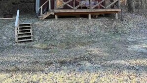 Una cabaña rústica con terraza de madera y porche, rodeada de árboles.