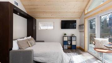 A bedroom with a bed, a sofa, a TV, a window, and a sliding glass door to a balcony.