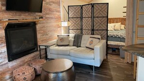 A cozy living room with a fireplace, a sofa, a coffee table, and a TV mounted on the wall. - Bugsy’s Escape House|Private|Nature (Lake Arrowhead)