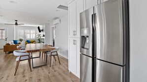 Een moderne keuken met witte kasten, een roestvrijstalen koelkast en een houten eettafel met stoelen.