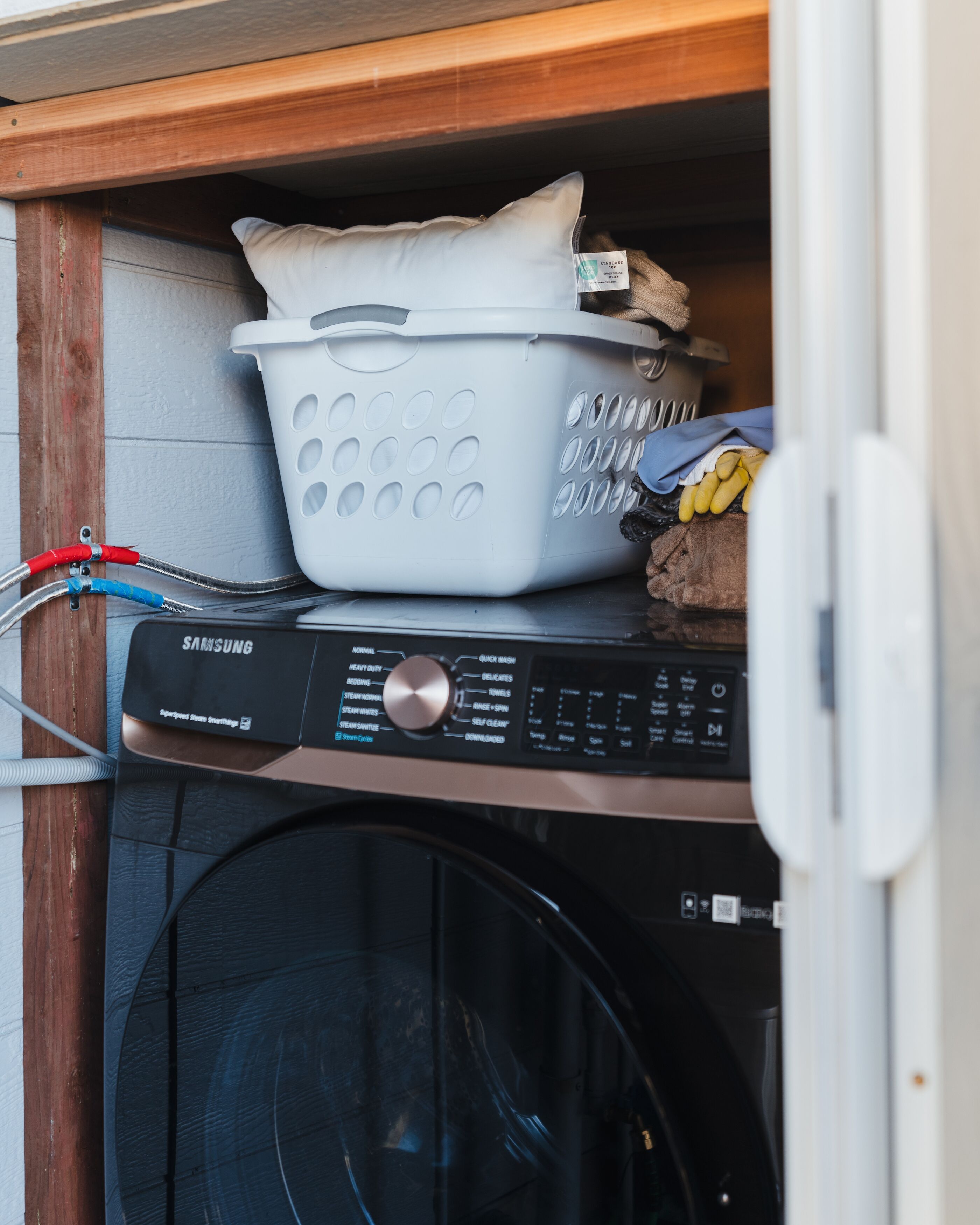 A washing machine with a control panel, a white laundry basket, and a pair of yellow gloves on top.
