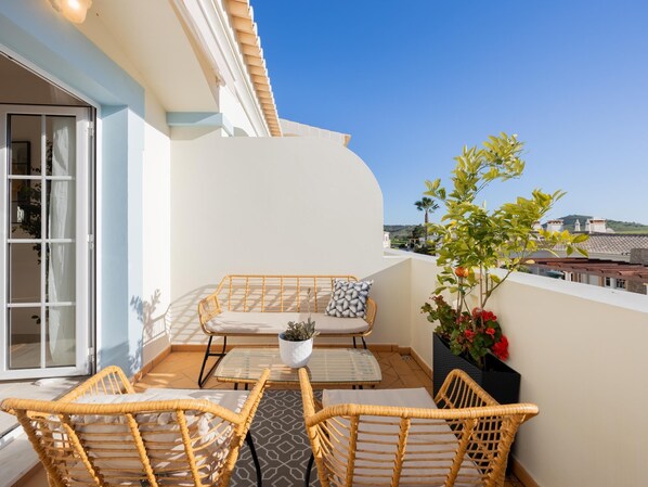 A balcony with wicker furniture, a glass table, and a potted plant.