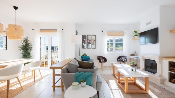 Un salon moderne comprenant un canapé, une table basse et un coin repas. On y trouve une cheminée et un téléviseur fixé au mur.
