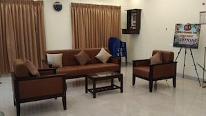 A living room with a brown sofa, two armchairs, a coffee table, and a small table with a vase. There is a sign on the wall and a blue chair in the corner.
