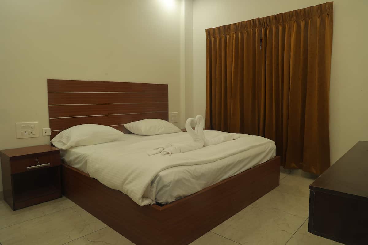 A neatly made bed with a wooden headboard, a small bedside table with a drawer, and a brown curtain on the window.