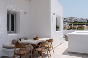 A white balcony with a table and chairs, a window, and a view of a white building complex. - Arotron Santorini (Santorini)