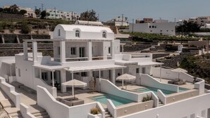 A white building with a pool, outdoor seating, and a view of the surrounding area. - Arotron Santorini (Santorini)