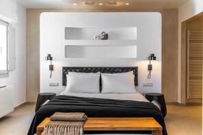 A modern bedroom with a bed, bedside tables, wall-mounted lights, and a wooden bench. - Arotron Santorini (Santorini)