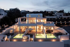 A modern multi-story house with a pool area, outdoor seating, and a well-lit entrance. - Arotron Santorini (Santorini)