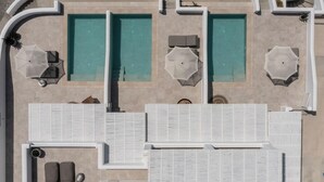 An aerial view of a hotel with multiple swimming pools, sun loungers, and a large covered area. - Arotron Santorini (Santorini)