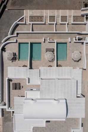 An aerial view of a hotel with multiple swimming pools, sun loungers, and a large covered area. - Arotron Santorini (Santorini)