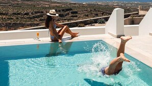 A pool with clear water, a person sitting, and another person diving. - Arotron Santorini (Santorini)