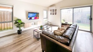 A modern living room with a leather sofa, a flat-screen TV, and a large sliding glass door leading to a backyard.