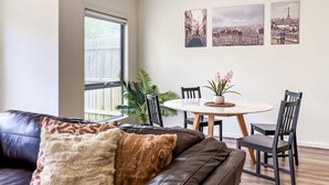 A living room with a leather sofa, a dining table with chairs, and a window with a view of buildings.