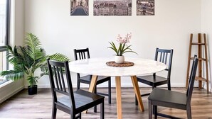 A dining area with a round table, six chairs, a potted plant, and three framed cityscape pictures on the wall.