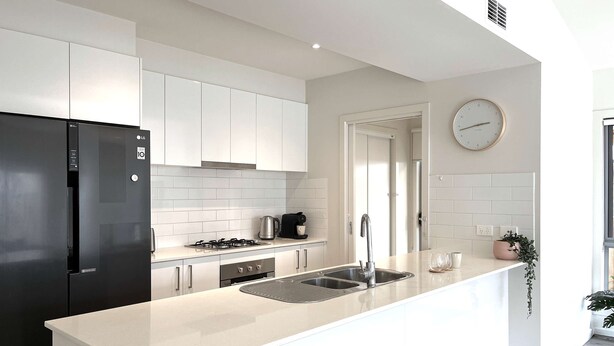 A modern kitchen with a black refrigerator, white cabinets, a gas stove, and a sink.