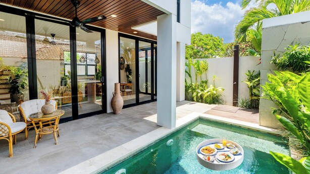 Un espace piscine extérieur moderne, agréé d’un coin repas, entouré d’une végétation luxuriante et surplombé d’un ciel dégagé.