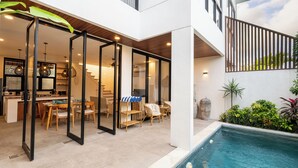 Une maison moderne dotée d’une piscine, d’un espace de vie et d’une salle à manger à aire ouverte, et d’un escalier menant à l’étage supérieur.