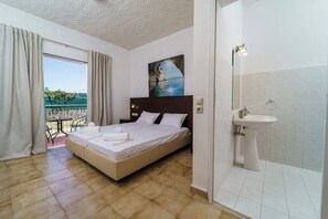 A hotel room with a bed, a bathroom with a sink, and a painting of a coastal scene. - Mayo Rooms (Zakynthos)