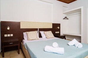 A hotel room with a bed, a nightstand, a wall-mounted shelf, and a towel rack.