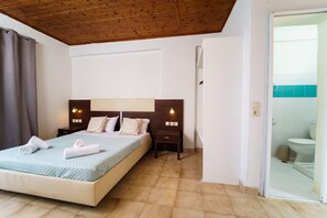 A bedroom with a bed, bedside tables, a nightstand, a wooden ceiling, and a bathroom visible through an open door.