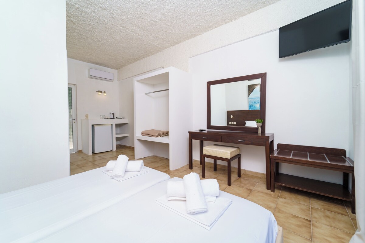 A hotel room with a bed, a desk, a chair, a television, and a small table.