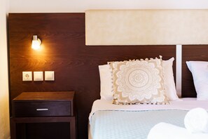 A hotel room with a wooden headboard, a bedside lamp, a nightstand, and a decorative pillow. - Mayo Rooms (Zakynthos)