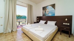 A double bed with white linens, a wooden headboard, a nightstand with a lamp, and a painting of a coastal scene. - Mayo Rooms (Zakynthos)